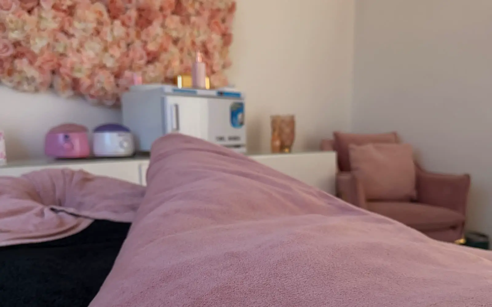 Treatment bed with a blush cover and flower wall at Fabulook Beauty, Arrington